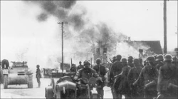 German infantry marches towards Brno, supported by a Pz.Kpfw. II Ausf. C light tank.
